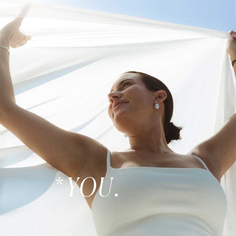 Frau hebt weißen Stoff in die Luft, lächelt im Sonnenlicht.